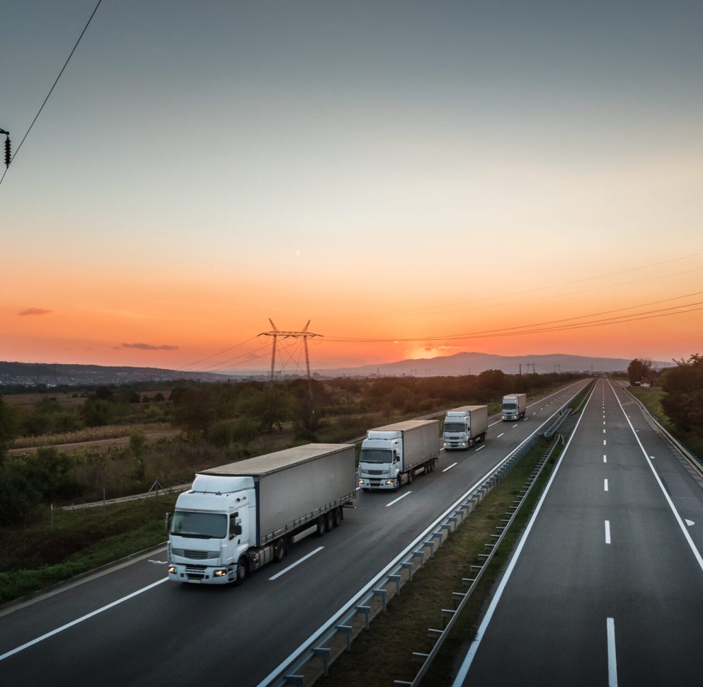 Four White Lorry Trucks Convoy on highway at beautiful sunset