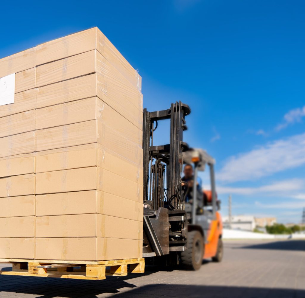 Forklift vehicle manipulating goods in logistic area outside warehouse.