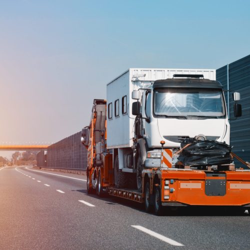A side view of the towing truck with a brand-new commercial vehicle. Emergency roadside assistance. Vehicle Mechanical Problem on the Road. A side view of the towing truck with a brand-new commercial vehicle. Emergency roadside assistance. Vehicle Mechanical Problem on the Road.